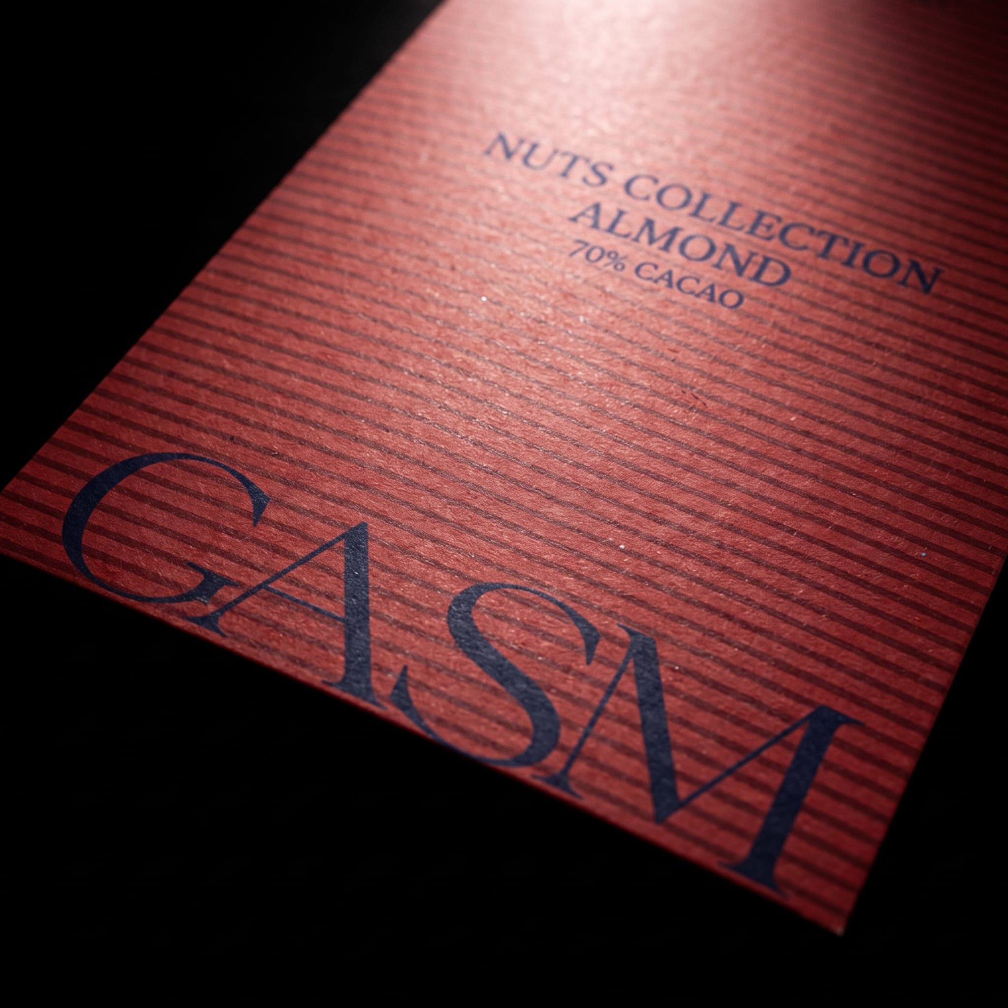 An angled close-up of the red ribbed sleeve, navy type reading Nuts Collection, Almond, 70% cacao.